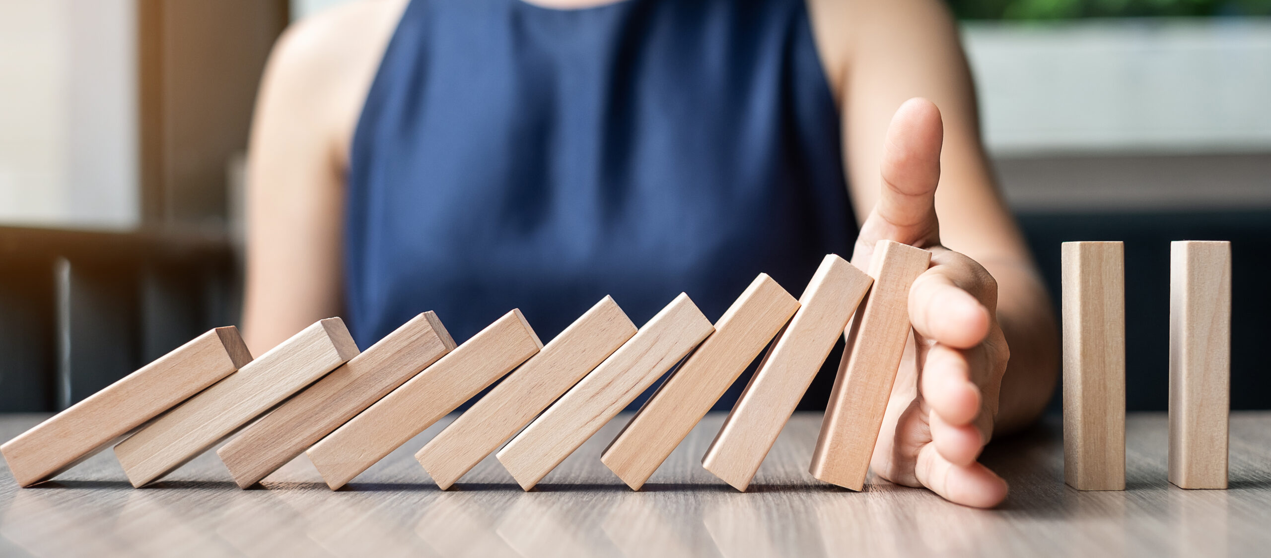 Businesswoman hand Stopping Falling wooden Dominoes